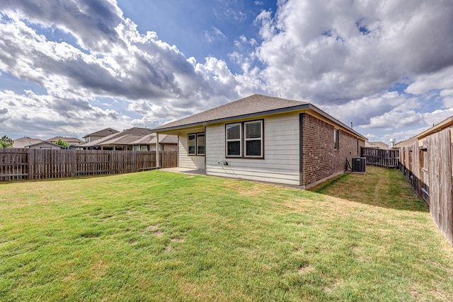 back of property featuring cooling unit, a lawn, a fenced backyard, and brick siding