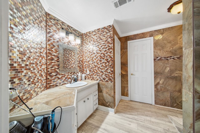 bathroom with tile walls, visible vents, wood finished floors, crown molding, and vanity