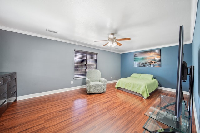 bedroom with wood finished floors, visible vents, crown molding, and baseboards