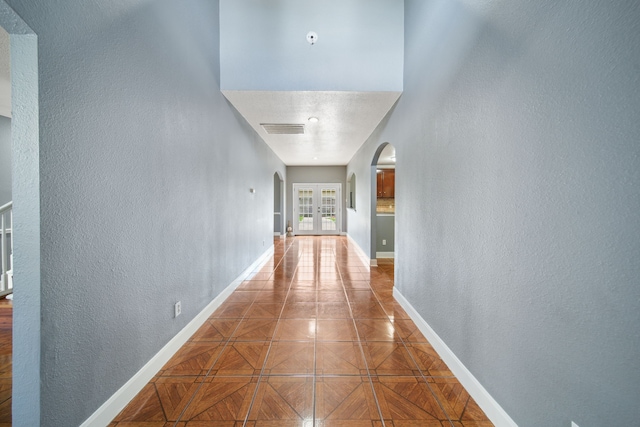hallway featuring visible vents, a textured wall, baseboards, and arched walkways