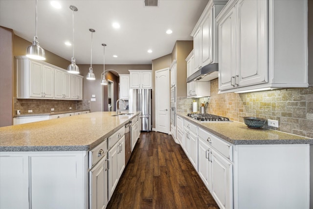 kitchen with under cabinet range hood, a sink, arched walkways, appliances with stainless steel finishes, and white cabinetry