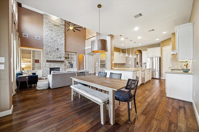 dining room with arched walkways, visible vents, a fireplace, and dark wood finished floors