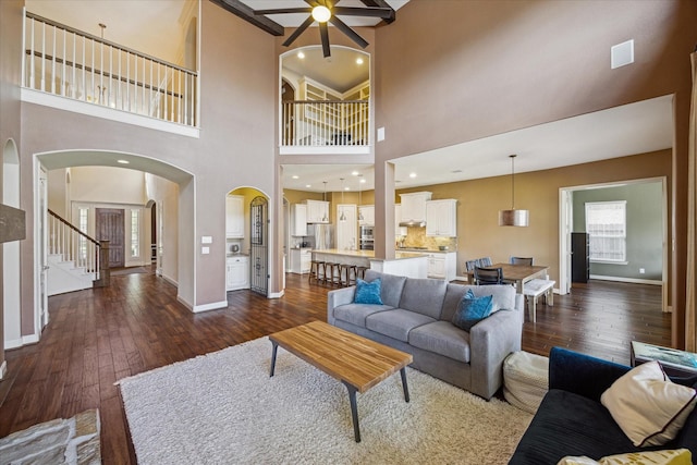 living area with arched walkways, baseboards, a ceiling fan, and dark wood-style floors