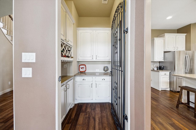 interior space with white cabinets, dark wood-style floors, light stone counters, and freestanding refrigerator
