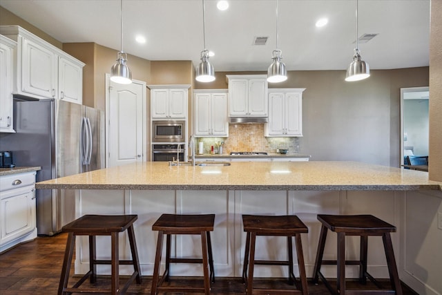 kitchen featuring under cabinet range hood, stainless steel appliances, visible vents, a sink, and tasteful backsplash
