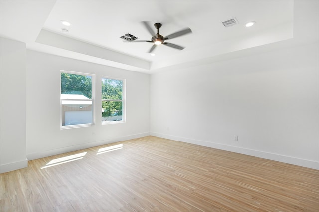 unfurnished room with light wood-type flooring, baseboards, visible vents, ceiling fan, and a raised ceiling