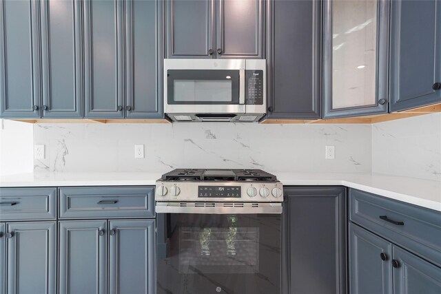 kitchen with light countertops, glass insert cabinets, appliances with stainless steel finishes, and decorative backsplash