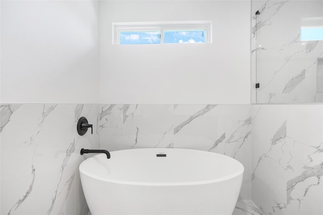 bathroom with tile walls, plenty of natural light, a freestanding tub, and marble finish floor