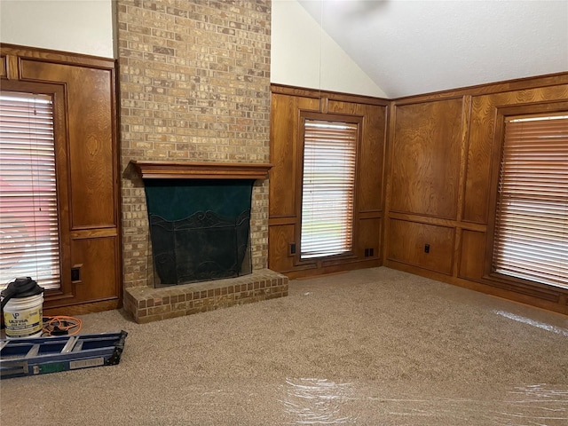 unfurnished living room with a fireplace, lofted ceiling, carpet floors, and wood walls