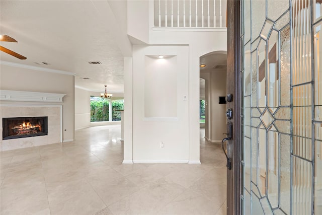 entryway featuring baseboards, arched walkways, ornamental molding, a fireplace, and ceiling fan with notable chandelier