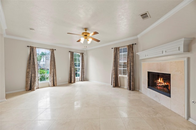 unfurnished living room with crown molding, visible vents, baseboards, a tiled fireplace, and a ceiling fan