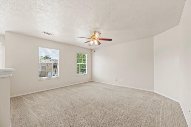 carpeted empty room featuring a textured ceiling, ceiling fan, baseboards, and visible vents