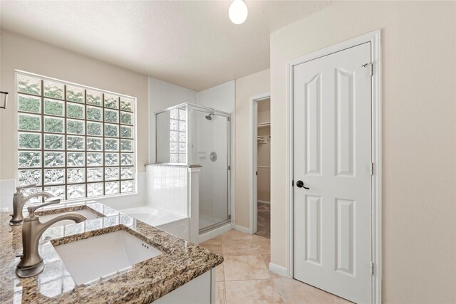 bathroom featuring tile patterned flooring, vanity, a walk in closet, a stall shower, and a textured ceiling