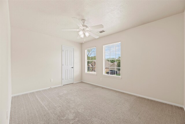empty room with a ceiling fan, visible vents, light colored carpet, and baseboards