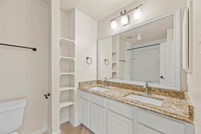 bathroom with baseboards, toilet, double vanity, and a sink