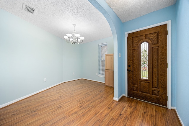 entrance foyer with a textured ceiling, wood finished floors, visible vents, and a notable chandelier