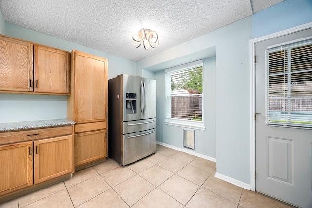 kitchen with stainless steel fridge, a textured ceiling, baseboards, light stone countertops, and light tile patterned floors