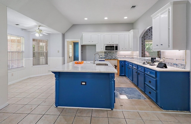 kitchen featuring a ceiling fan, blue cabinets, a sink, stainless steel microwave, and a wainscoted wall
