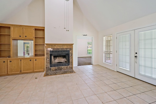 unfurnished living room featuring a tiled fireplace, high vaulted ceiling, light tile patterned floors, and french doors
