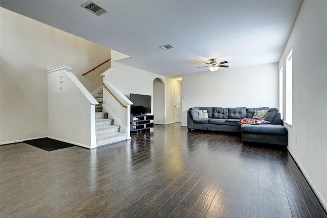 living area with arched walkways, a ceiling fan, wood finished floors, visible vents, and stairway