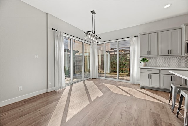 unfurnished dining area featuring a chandelier, a healthy amount of sunlight, light wood finished floors, and baseboards