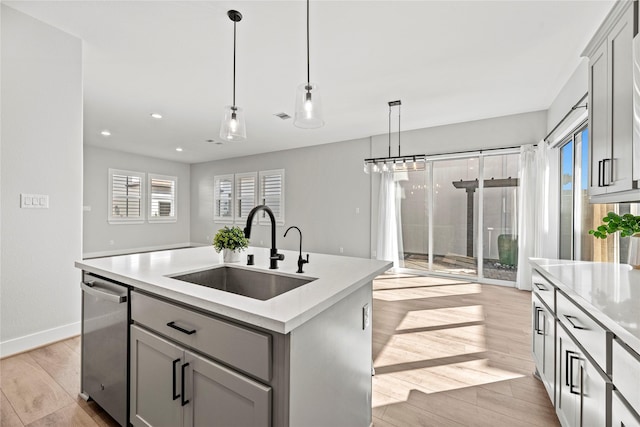 kitchen featuring light countertops, stainless steel dishwasher, a sink, a center island with sink, and light wood-style flooring