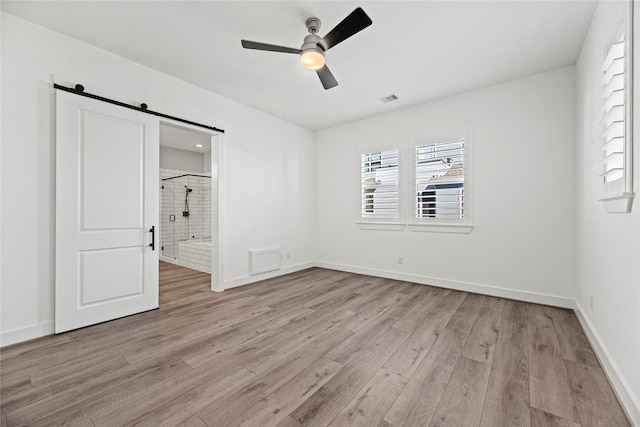 unfurnished bedroom with a barn door, ceiling fan, light wood finished floors, baseboards, and visible vents