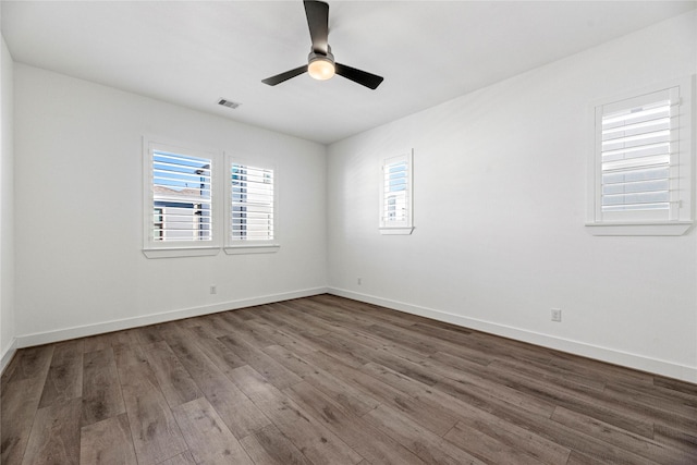 spare room featuring a ceiling fan, wood finished floors, visible vents, and plenty of natural light