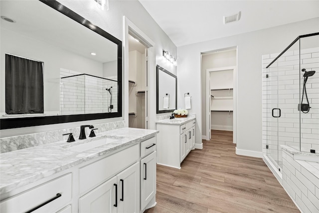 full bathroom with a shower stall, wood finished floors, a spacious closet, vanity, and visible vents