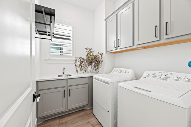 laundry area with cabinet space, light wood-style floors, washer and dryer, and a sink