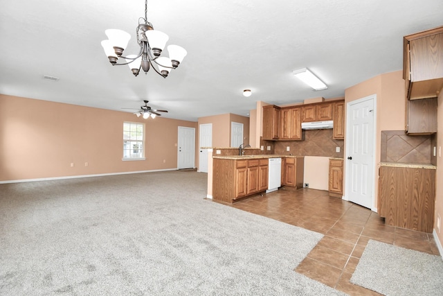 kitchen featuring under cabinet range hood, backsplash, white dishwasher, baseboards, and ceiling fan with notable chandelier