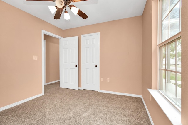 unfurnished bedroom featuring carpet floors, a ceiling fan, baseboards, and multiple windows