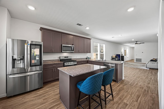 kitchen featuring visible vents, a sink, a center island, a peninsula, and appliances with stainless steel finishes