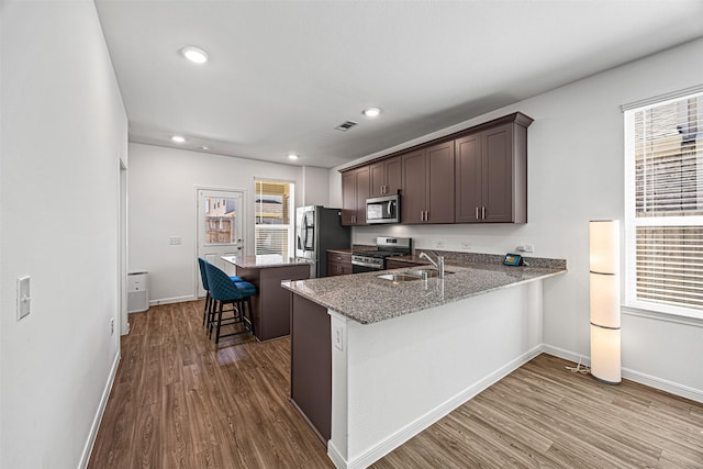 kitchen featuring a sink, dark brown cabinetry, a kitchen bar, appliances with stainless steel finishes, and dark wood-style flooring