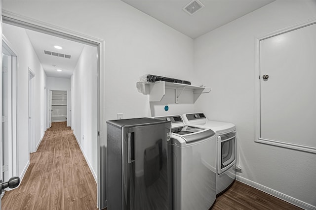 washroom with separate washer and dryer, visible vents, wood finished floors, and laundry area