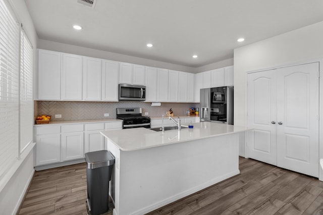 kitchen with backsplash, wood finished floors, light countertops, stainless steel appliances, and white cabinetry