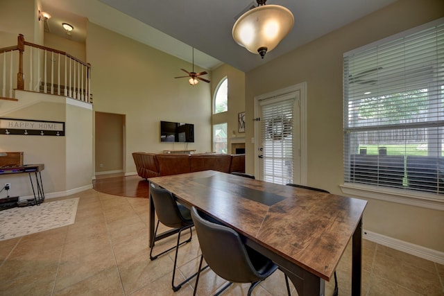 dining space with light tile patterned flooring, ceiling fan, baseboards, and a fireplace