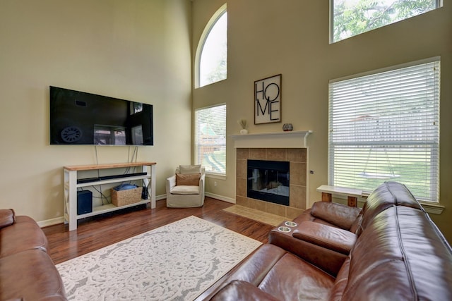 living room with a towering ceiling, a tile fireplace, wood finished floors, and plenty of natural light