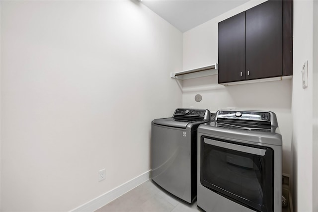 laundry area with washing machine and dryer, baseboards, cabinet space, and light tile patterned floors