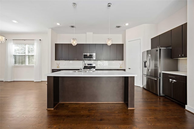kitchen featuring stainless steel appliances, light countertops, a sink, decorative light fixtures, and tasteful backsplash