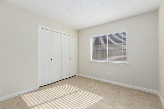 5442 Garden Village Dr, Kingwood, TX 77339 - unfurnished bedroom with light tile patterned flooring, a textured ceiling, a closet, and baseboards