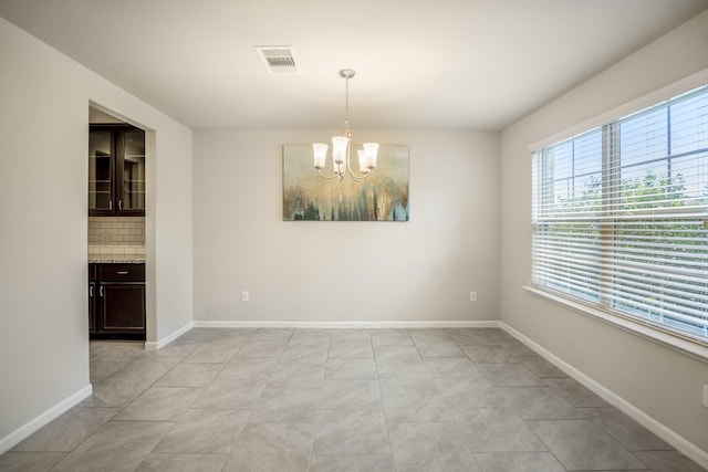 unfurnished dining area featuring baseboards, visible vents, and a chandelier