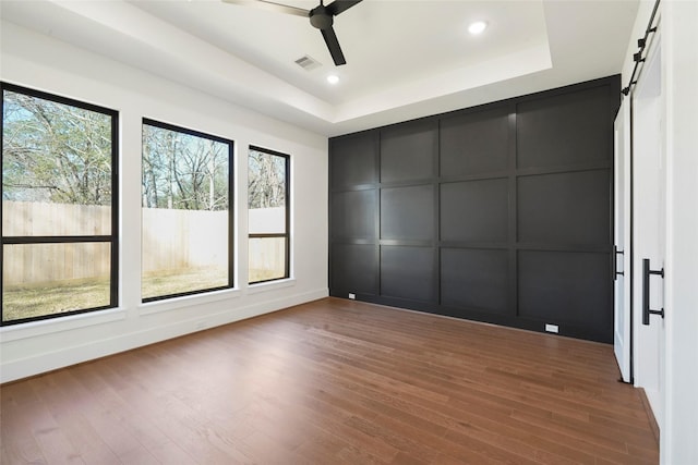 1957 Restridge Dr, Houston, TX 77055 - unfurnished bedroom featuring a decorative wall, multiple windows, a raised ceiling, wood finished floors, and a barn door