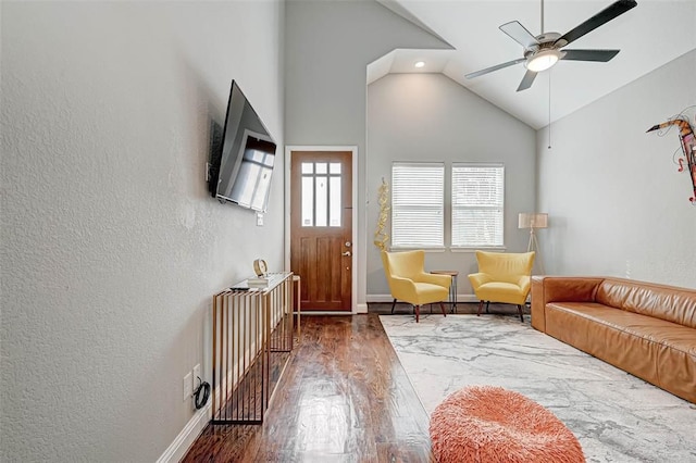 interior space featuring baseboards, wood finished floors, ceiling fan, a textured wall, and high vaulted ceiling