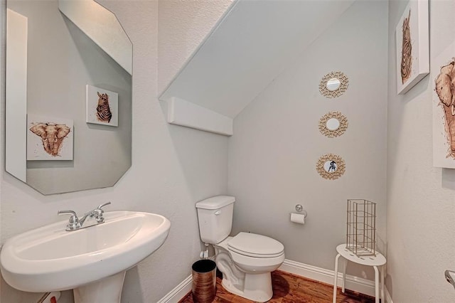 half bath featuring lofted ceiling, wood finished floors, toilet, a sink, and baseboards