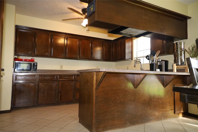 9948 Twin Shores Dr, Willis, TX 77318 - kitchen with light tile patterned flooring, stainless steel microwave, dark brown cabinetry, and a ceiling fan