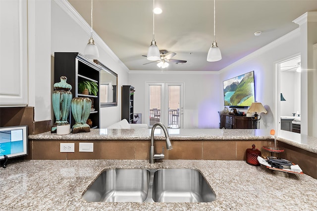 kitchen featuring a ceiling fan, ornamental molding, a sink, decorative light fixtures, and light stone countertops