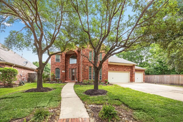 traditional-style home featuring a garage, a front lawn, fence, and concrete driveway