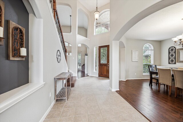 tiled entrance foyer with an inviting chandelier, baseboards, a high ceiling, stairway, and arched walkways
