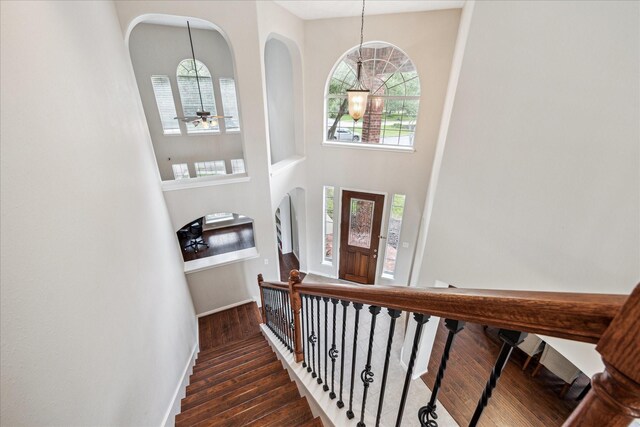 stairs with a healthy amount of sunlight, arched walkways, wood finished floors, baseboards, and a high ceiling